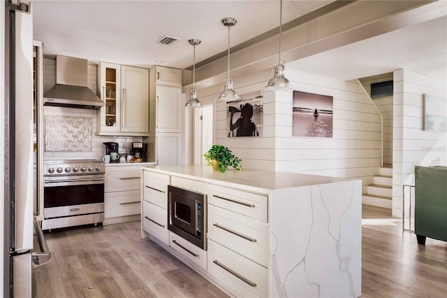 kitchen with stainless steel appliances, wood-type flooring, pendant lighting, and wall chimney exhaust hood