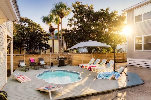 pool at dusk featuring a wooden deck and grilling area