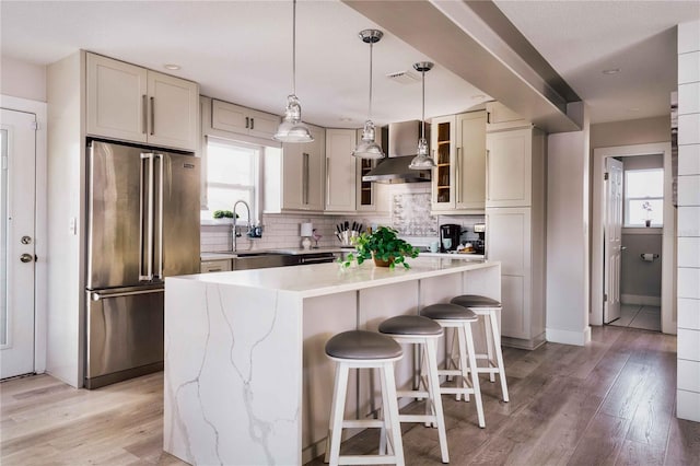 kitchen featuring sink, decorative light fixtures, high quality fridge, a kitchen island, and wall chimney range hood