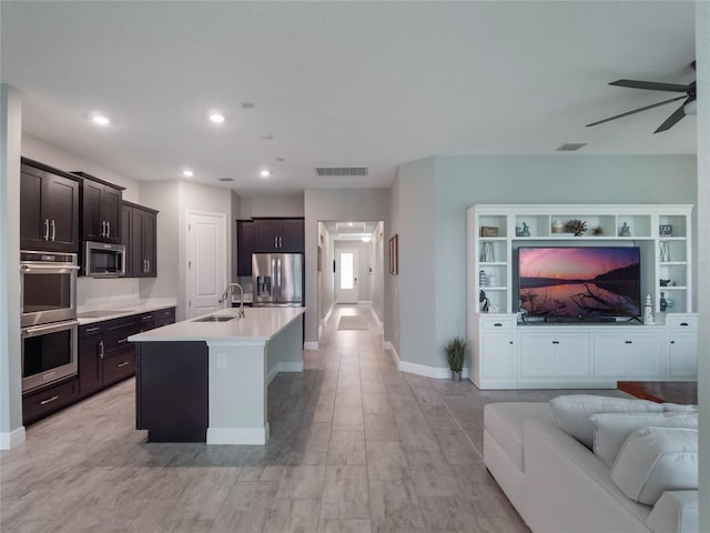 kitchen featuring appliances with stainless steel finishes, sink, a kitchen island with sink, ceiling fan, and dark brown cabinets