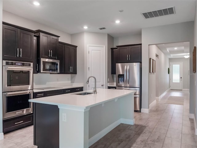 kitchen featuring sink, an island with sink, dark brown cabinets, and appliances with stainless steel finishes