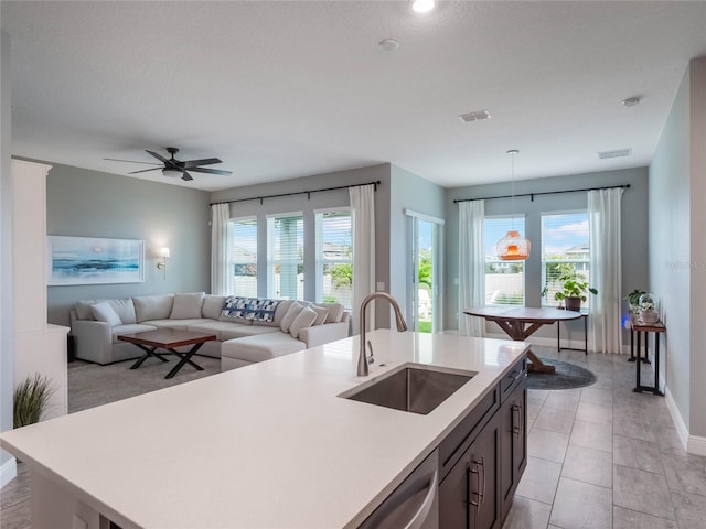 kitchen featuring dishwasher, light tile patterned floors, sink, pendant lighting, and an island with sink