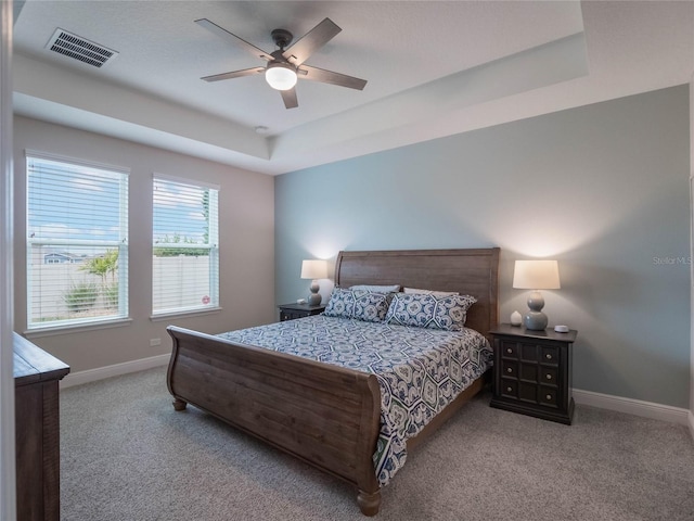 carpeted bedroom with ceiling fan and a raised ceiling