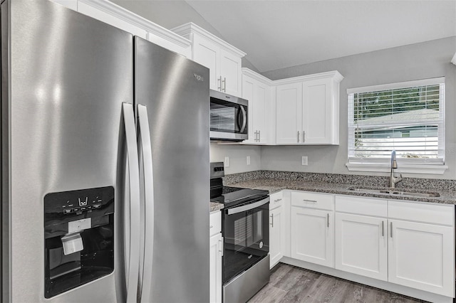 kitchen with appliances with stainless steel finishes, light wood-type flooring, dark stone counters, white cabinets, and sink