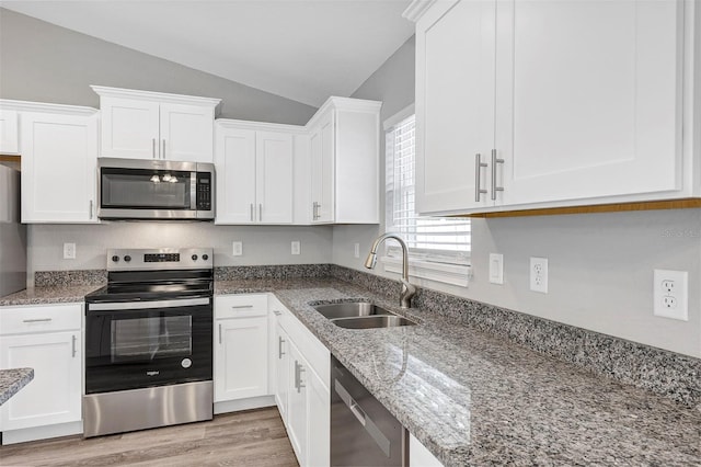 kitchen with light stone countertops, white cabinets, appliances with stainless steel finishes, sink, and vaulted ceiling