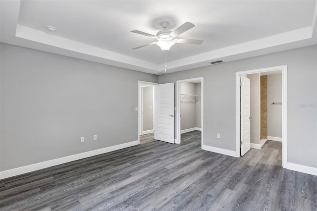 unfurnished bedroom featuring a raised ceiling, a walk in closet, ceiling fan, and a closet