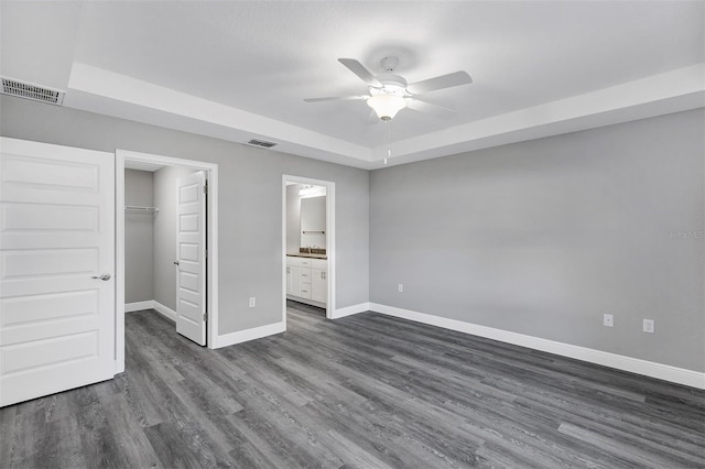 unfurnished bedroom with ensuite bath, a walk in closet, a closet, ceiling fan, and a tray ceiling