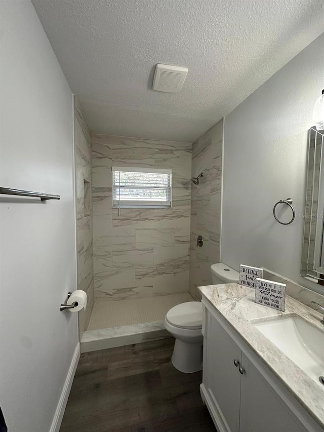 bathroom with a textured ceiling, hardwood / wood-style floors, vanity, toilet, and tiled shower