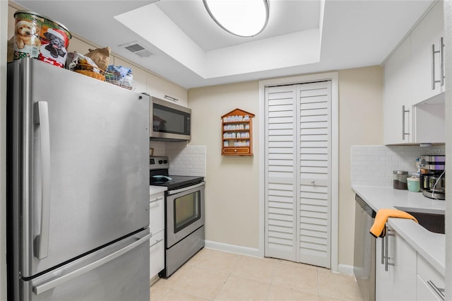 kitchen featuring light tile patterned floors, white cabinetry, appliances with stainless steel finishes, a raised ceiling, and tasteful backsplash