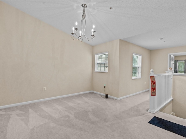 carpeted spare room with a chandelier and a textured ceiling