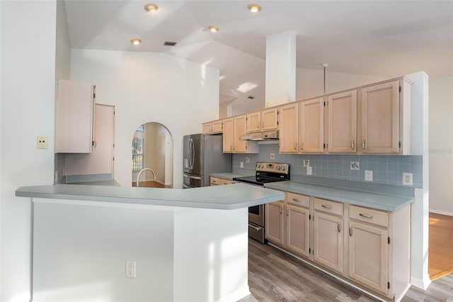 kitchen with vaulted ceiling, stainless steel appliances, decorative backsplash, kitchen peninsula, and light wood-type flooring