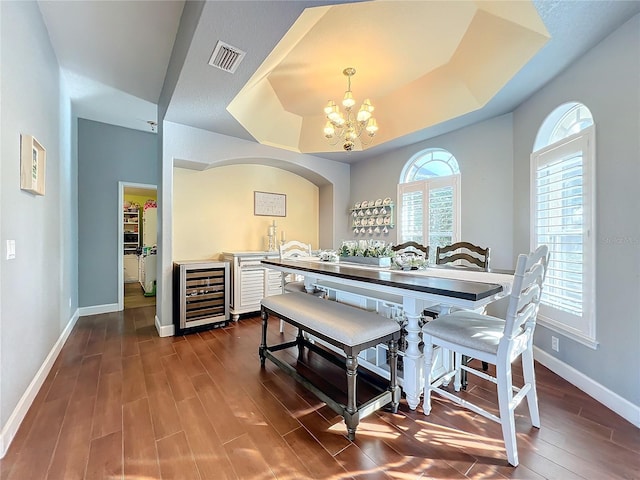 dining space featuring dark hardwood / wood-style flooring, beverage cooler, a tray ceiling, and a chandelier