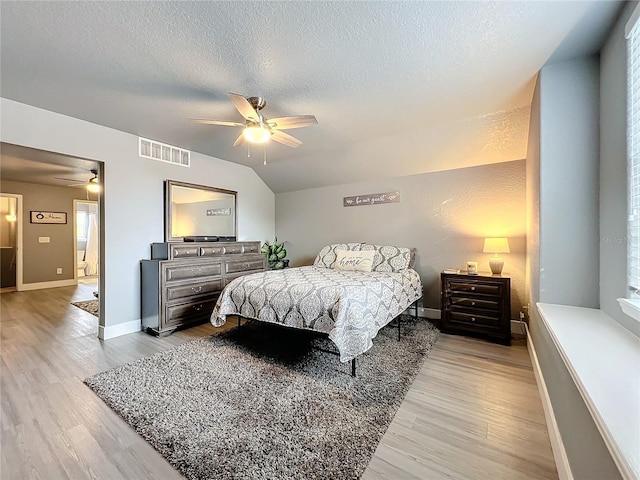 bedroom featuring a textured ceiling, light wood-type flooring, multiple windows, vaulted ceiling, and ceiling fan