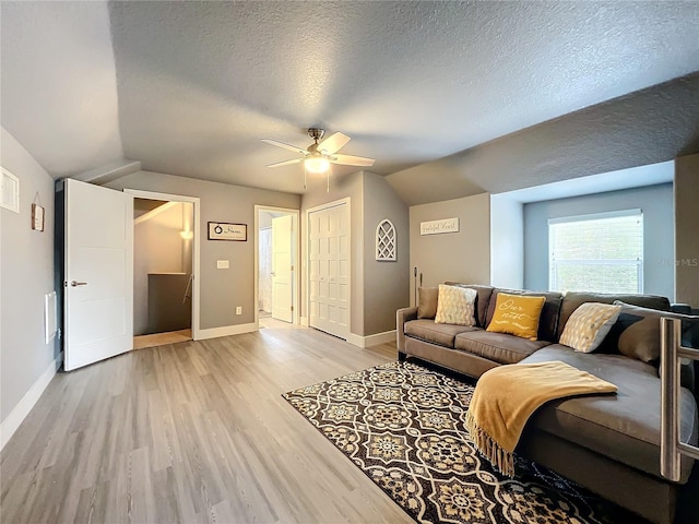 living room featuring ceiling fan, a textured ceiling, light hardwood / wood-style flooring, and vaulted ceiling