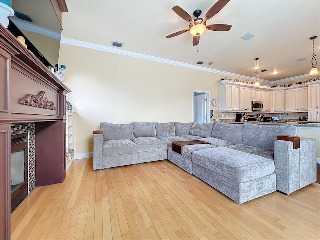 living room with ceiling fan, light wood-type flooring, a fireplace, crown molding, and sink