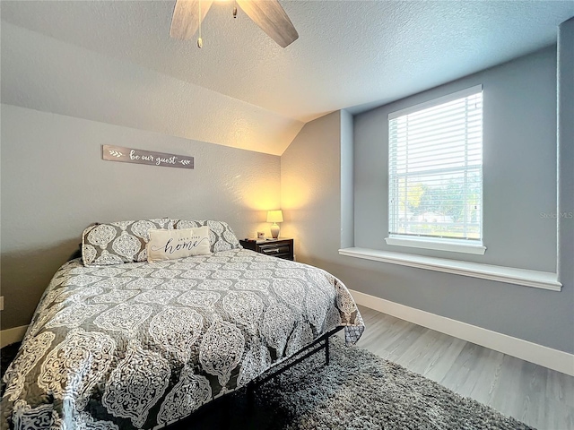 bedroom with vaulted ceiling, ceiling fan, a textured ceiling, and hardwood / wood-style floors