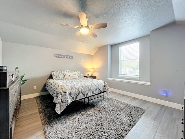 bedroom with ceiling fan, a textured ceiling, lofted ceiling, and light wood-type flooring