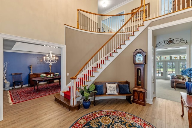 stairs featuring hardwood / wood-style flooring, a high ceiling, a notable chandelier, crown molding, and french doors