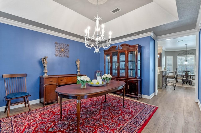 dining room featuring an inviting chandelier, ornamental molding, a tray ceiling, and light hardwood / wood-style flooring