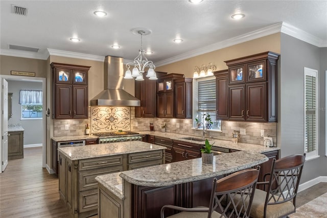 kitchen featuring pendant lighting, sink, a center island, stainless steel gas cooktop, and wall chimney range hood