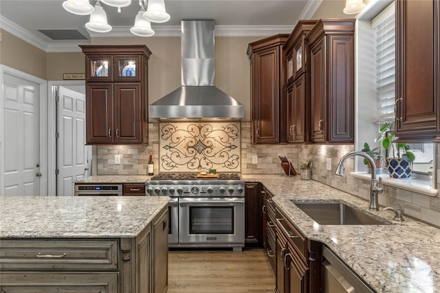 kitchen featuring sink, hanging light fixtures, appliances with stainless steel finishes, light stone countertops, and wall chimney range hood