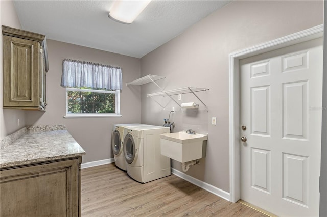 laundry area with washer and dryer, sink, light wood-type flooring, cabinets, and a textured ceiling