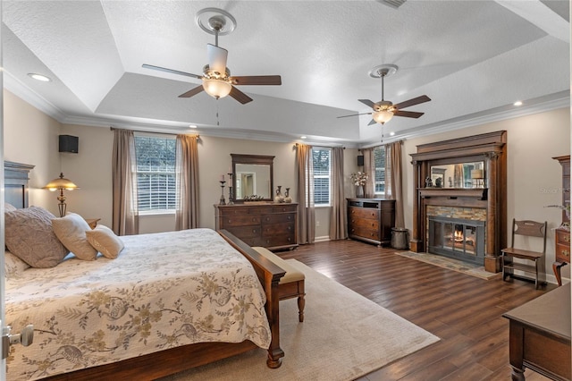 bedroom featuring dark wood-type flooring, a textured ceiling, ornamental molding, a tray ceiling, and a fireplace