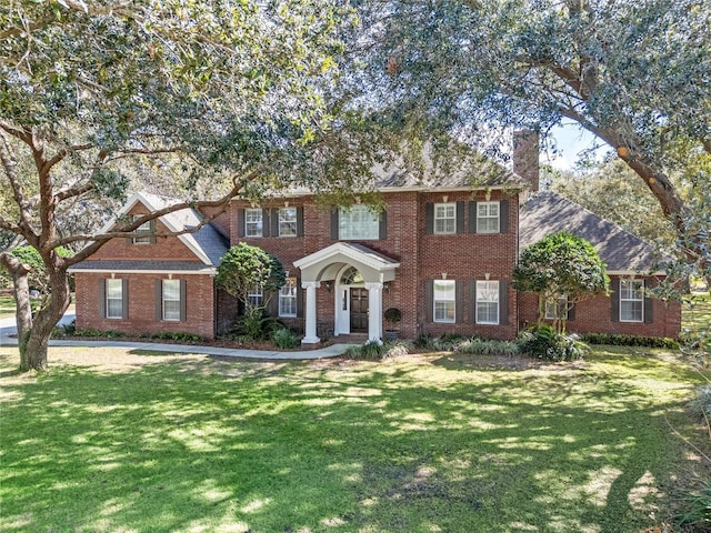 view of front of house featuring brick siding, a chimney, and a front lawn