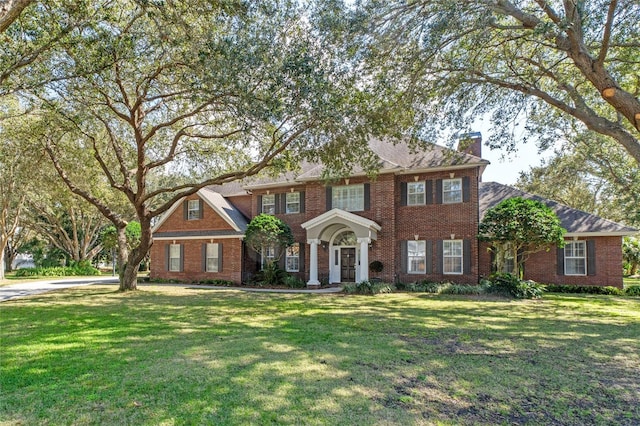 georgian-style home with a chimney, a front lawn, and brick siding