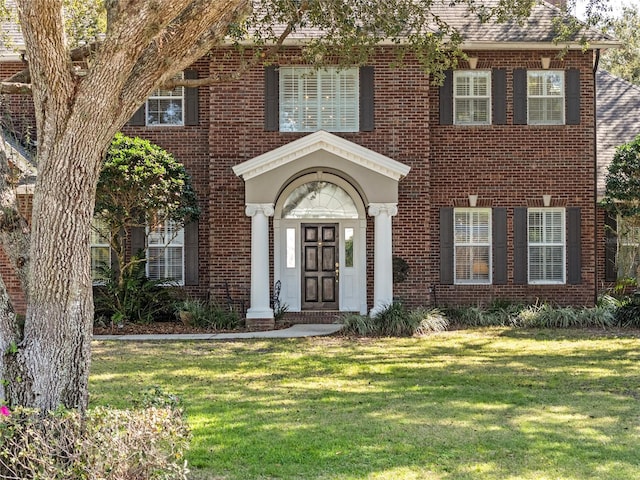 view of front of property featuring a front lawn, roof with shingles, and brick siding