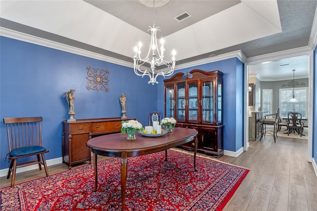 dining space with baseboards, ornamental molding, hardwood / wood-style floors, a tray ceiling, and a notable chandelier