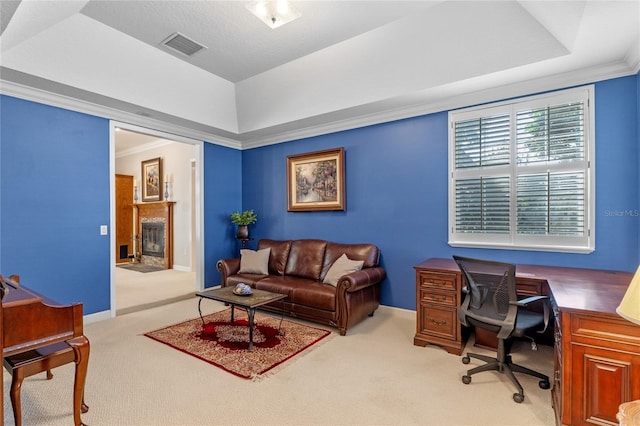 carpeted home office featuring visible vents, a raised ceiling, crown molding, and a glass covered fireplace