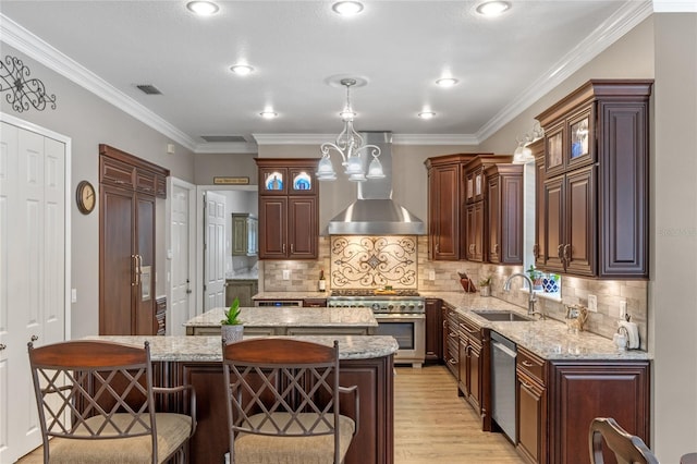 kitchen featuring wall chimney exhaust hood, light stone counters, a center island, stainless steel appliances, and a sink