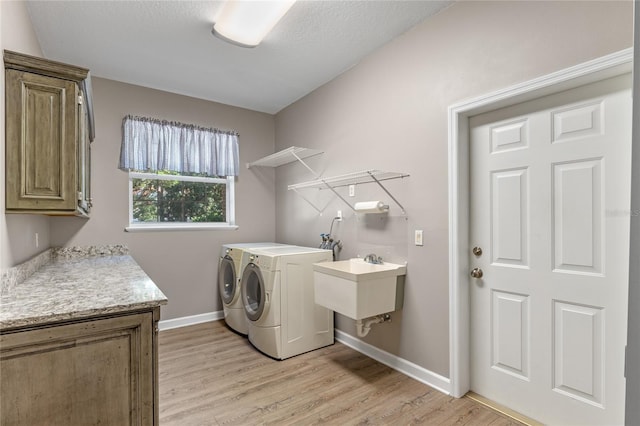 clothes washing area with light wood-type flooring, cabinet space, baseboards, and washer and clothes dryer