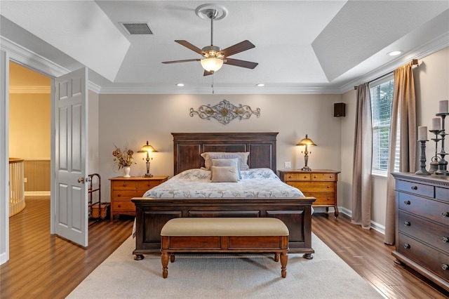 bedroom featuring wood finished floors, visible vents, baseboards, a raised ceiling, and crown molding