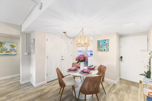 dining room featuring sink, light hardwood / wood-style floors, a textured ceiling, and a notable chandelier