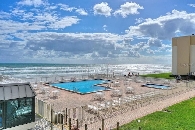 view of swimming pool with a patio, a water view, and a beach view