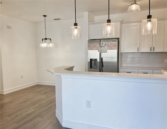 kitchen featuring stainless steel refrigerator with ice dispenser, light hardwood / wood-style flooring, hanging light fixtures, white cabinetry, and decorative backsplash