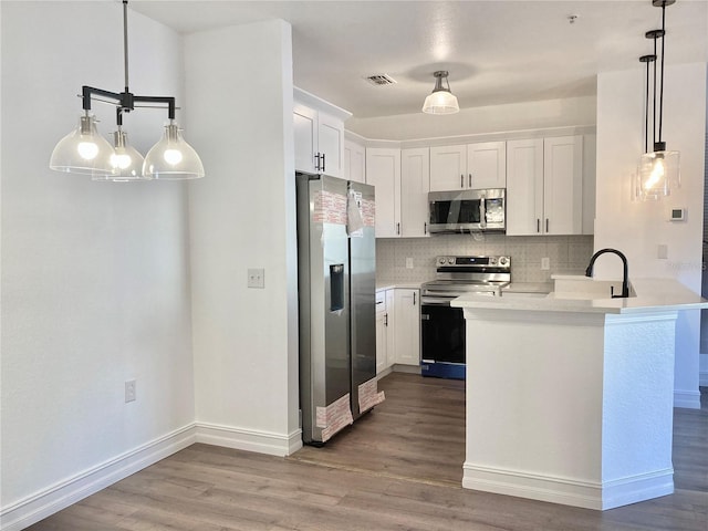 kitchen with kitchen peninsula, hanging light fixtures, tasteful backsplash, white cabinetry, and stainless steel appliances