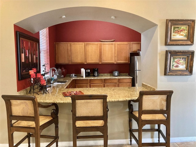 kitchen with light stone countertops, sink, a kitchen breakfast bar, and stainless steel refrigerator