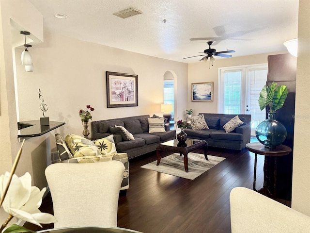 living room featuring ceiling fan, dark wood-type flooring, and a textured ceiling