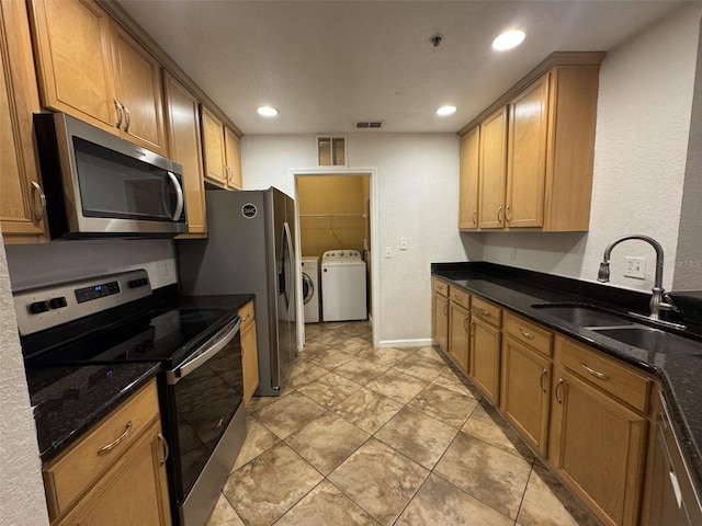 kitchen featuring sink, washing machine and clothes dryer, dark stone counters, and stainless steel appliances