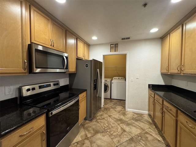 kitchen with stainless steel appliances, washer and clothes dryer, and dark stone counters