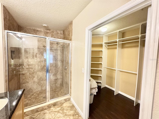 bathroom with a textured ceiling, tile patterned flooring, a shower with shower door, and vanity