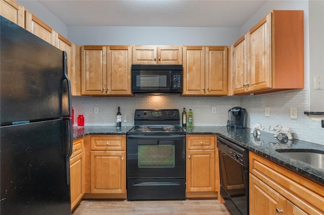 kitchen featuring dark stone countertops, black appliances, tasteful backsplash, and light hardwood / wood-style flooring