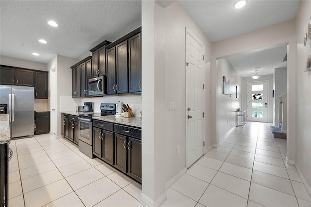 kitchen featuring light tile patterned floors, appliances with stainless steel finishes, backsplash, a textured ceiling, and light stone counters