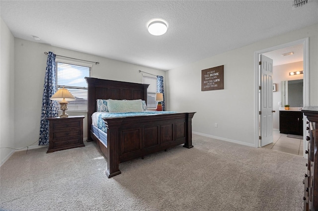 bedroom featuring ensuite bath, light carpet, and a textured ceiling