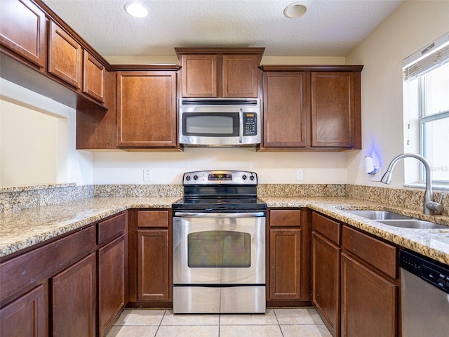 kitchen with sink, light tile patterned floors, appliances with stainless steel finishes, light stone countertops, and a textured ceiling