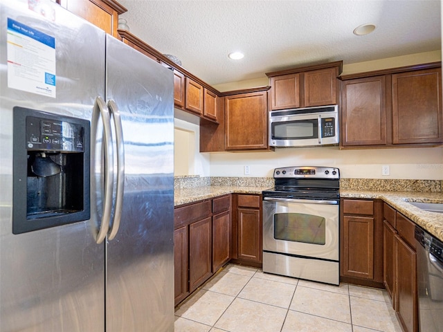 kitchen with light tile patterned floors, light stone countertops, a textured ceiling, and appliances with stainless steel finishes