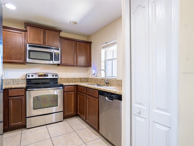 kitchen featuring sink, light tile patterned floors, light stone countertops, and appliances with stainless steel finishes